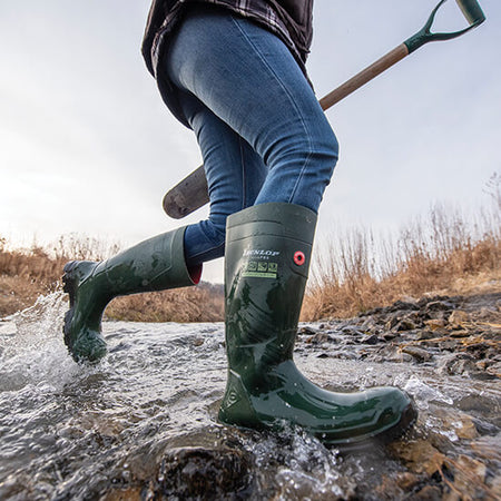 Close-up image of a person running through a rocky stream wearing a pair of green Dunlop TerraPRO wellingtons