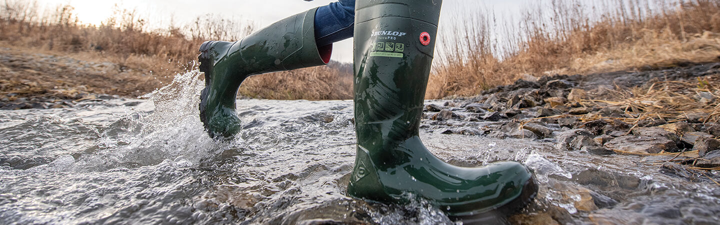 Close-up image of a person running through a rocky stream wearing a pair of green Dunlop TerraPRO wellingtons