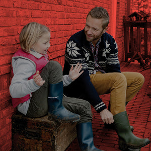 A father and daughter sat on a wooden bench talking to each other, wearing cold weather clothing and Dunlop wellington boots